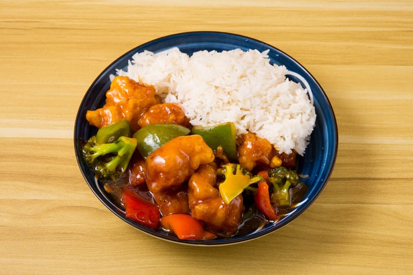 Sweet and sour chicken with bell peppers, broccoli, and white rice in a blue bowl.