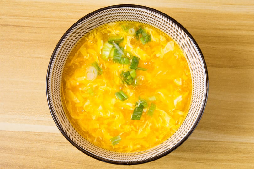 Overhead view of a bowl of golden egg drop soup garnished with chopped green onions.